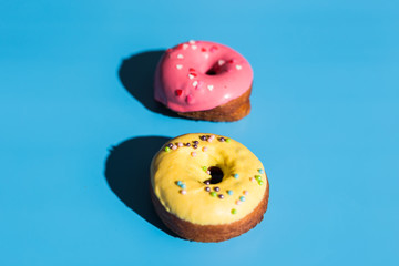 Colourful round donuts at bright blue background. Sweet donuts. Trendy sunlight Summer pattern Minimal summer concept.