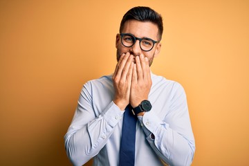 Young handsome businessman wearing tie and glasses standing over yellow background laughing and...