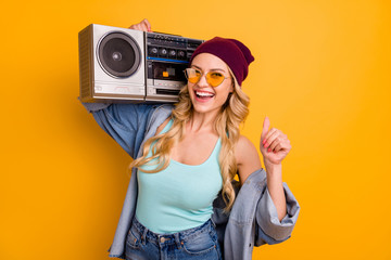 Photo of attractive lady long hairdo good mood free time hold shoulder vintage tape recorder wear casual turquoise singlet denim shirt sun specs headwear isolated yellow color background