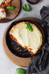 Shepherd's pie. Traditional British meal with minced meat, mashed potatoes and vegetables in cast iron pan. Autumn dinner, comfort food. Grey stone background, selective focus. Top view.