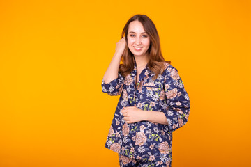 Excited young woman with curly hair in home wear pajama, widely smiling having fun. Isolated on yellow background. Copy space.