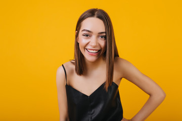 Laughing female model in black tank-top isolated on yellow background. Studio portrait of carefree brunette woman with pretty smile.