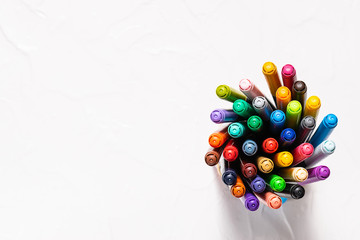Set of multicolored markers on white stone background top view, copy space for your design. Back to school and education concept.