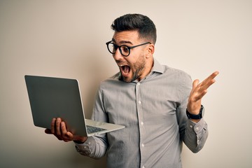 Young business man wearing glasses working using computer laptop very happy and excited, winner expression celebrating victory screaming with big smile and raised hands