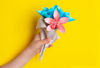 Children`s hand holds a bouquet of paper flowers made using the origami technique on a yellow...
