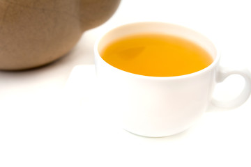 White porcelain cup with green tea with old light brown clay teapot with cracks and scratches on white background.