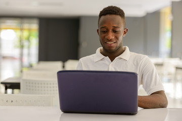 Portrait of happy young African man using laptop inside modern building