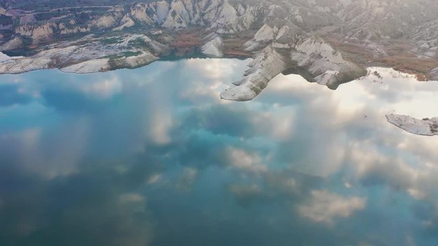 Reflejo sobre el agua de un pantano rodeado de monta&ntilde;as las nubes y el cielo.