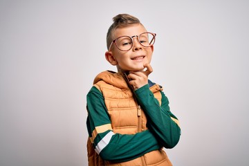 Young little caucasian kid with blue eyes wearing winter coat and smart glasses looking confident at the camera with smile with crossed arms and hand raised on chin. Thinking positive.