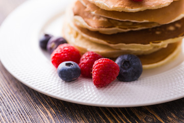 Pile of pancakes with blueberries and raspberries for breakfast on wooden table.