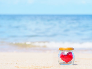 Close up red cushion heart shape in glass bottle on summer beach.