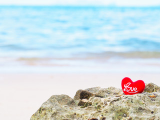 Close up red cushion heart shape with letter LOVE on summer beach.