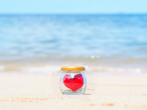 Close up red cushion heart shape in glass bottle on summer beach.