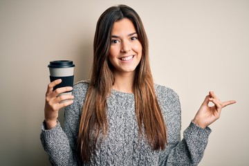 Young beautiful girl drinking cup of coffee standing over isolated white background very happy pointing with hand and finger to the side