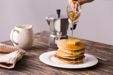 Male hand pouring maple syrup on tasty pancakes.