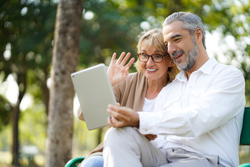 Obraz premium Happy senior elderly couple lifestyle technology chat communication internet video call and social media by tablet with friend or family while relax in park