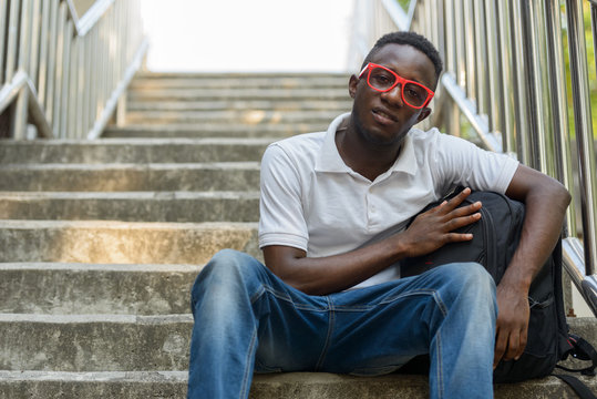 Young African man with backpack sitting at staircase in the city