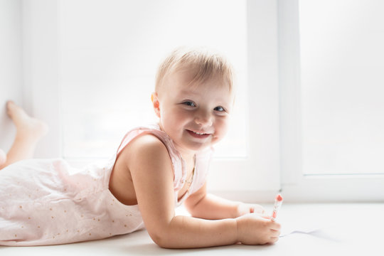 Caucasian baby girl lies and paints on windowsill