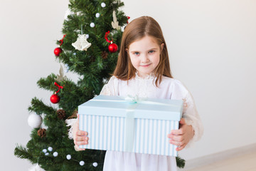 Child girl with gift box near Christmas tree. Holidays, christmas time and presents concept.