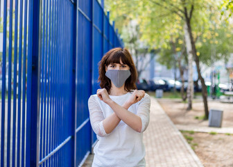 A girl in a medical mask stands on the street with her arms crossed. A young brunette girl shows a...