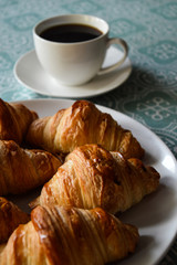 Homemade croissants on the white plate with cup of coffee in background