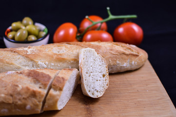 Artisan baguette sliced on the wooden board with olives and tomatoes in background, Mediterranean food