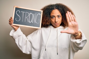 Young african american woman with afro hair holding blackboard with strong message with open hand doing stop sign with serious and confident expression, defense gesture