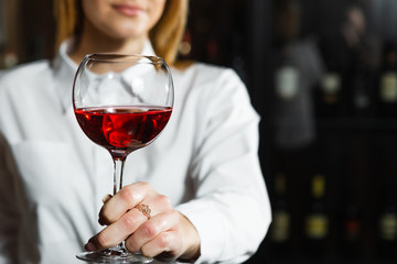 Close up photo of young beautiful blonde smilling girl sommelier is holding a glass of red wine. Sommelier smelling wine bouquet.