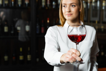 Close up photo of young beautiful blonde smilling girl sommelier is holding a glass of red wine. Sommelier smelling wine bouquet.