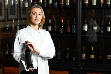 Young pretty girl sommelier serving & presenting bottles of red and white of wine. Appreciates the aroma of wine.