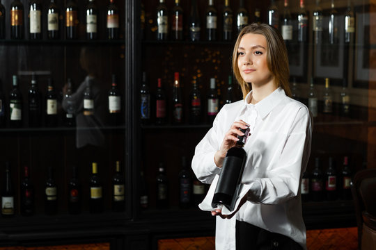 Young pretty girl sommelier serving & presenting bottles of red and white of wine. Appreciates the aroma of wine.