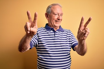 Grey haired senior man wearing casual navy striped t-shirt standing over yellow background smiling...