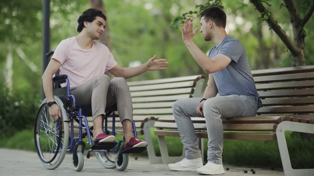 Young man in a wheelchair meet his friend in the park.