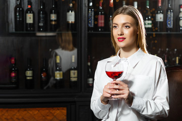 Young beautiful blonde smilling girl sommelier is holding a glass of red wine. Sommelier smelling wine bouquet.