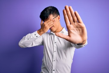 Young handsome business man wearing shirt and glasses over isolated purple background covering eyes with hands and doing stop gesture with sad and fear expression. Embarrassed and negative concept.