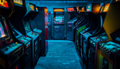 Arcade video games in an empty dark gaming room with purple light with glowing vintage displays and beautiful old retro design - obrazy, fototapety, plakaty