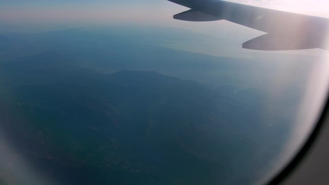 View of the Alps through the plane window. During the flight, you can see the wing, sun rays and a small fog