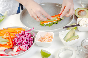 The process of making spring rolls. Healthy lunch preparation. Woman's hands putting sliced vegetables on the rice paper.