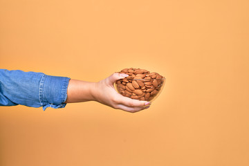 Beautiful hand of woman holding bowl with baked german pretzels over isolated yellow background