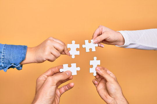 Hands of caucasian young people connecting pieces of puzzle over isolated yellow background