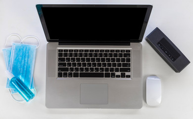 Top view Laptop, mouse, speaker, alcohols spray and Medical mask on white wood table. Work from home concept.