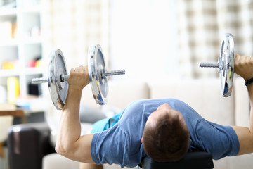 Close-up of strong fit person lifting metal heavy dumbbells at home. Cozy interior and necessary equipment to get stronger. Quarantine period. Sport and bodybuilder concept