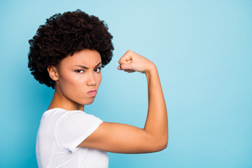 Fototapeta na wymiar Profile photo of beautiful dark skin curly lady showing perfect shape biceps after intense training gym harsh angry mood wear casual white t-shirt isolated blue color background
