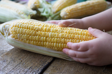 Hands holding corn on wooden table, dark mood