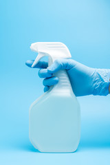 Hand in gloves hold disinfectant sprayer bottle isolated on blue background