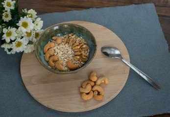 Oatmeal with cashews and walnuts and white flowers on a wooden tray and blue and white background. Healthy breakfast