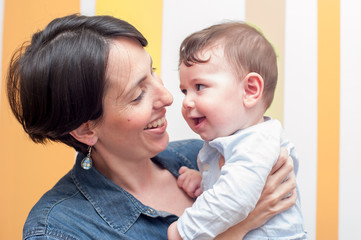 front view of a young mother lovely holding her baby boy, they are both smiling and looking for each other.