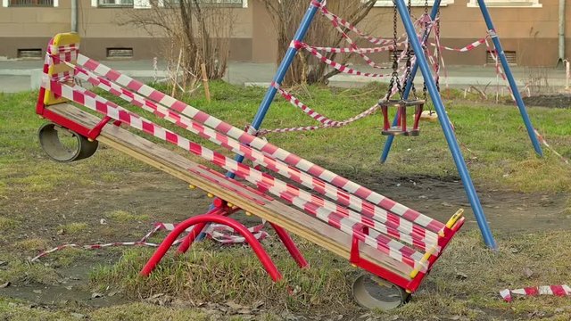 a closed children's Playground in a residential area with swings is wrapped in red banning ribbons