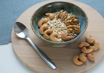 Oatmeal with cashews and walnuts on a wooden tray and blue and white background. Healthy breakfast