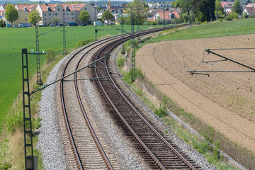 Two railway tracks leading through a landscape with green and brown fields. With bend / curve.